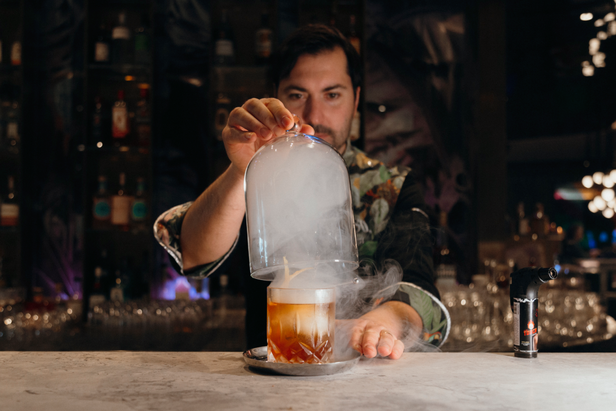 Giacomo Giannotti lifting the glass cover of the Great Gatsy, an Old-Fashioned style cocktail from Paradiso, which uses smoke.